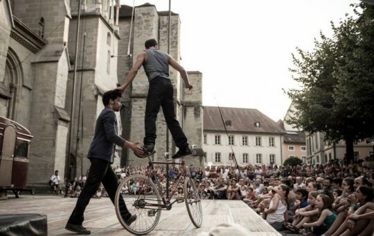 un homme sur un vélo sur scène tneu par un homme débout